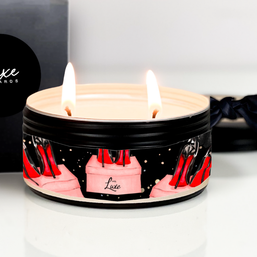 Candle in a decorative tin with red high heels and 'Luxe' text, on a white surface.