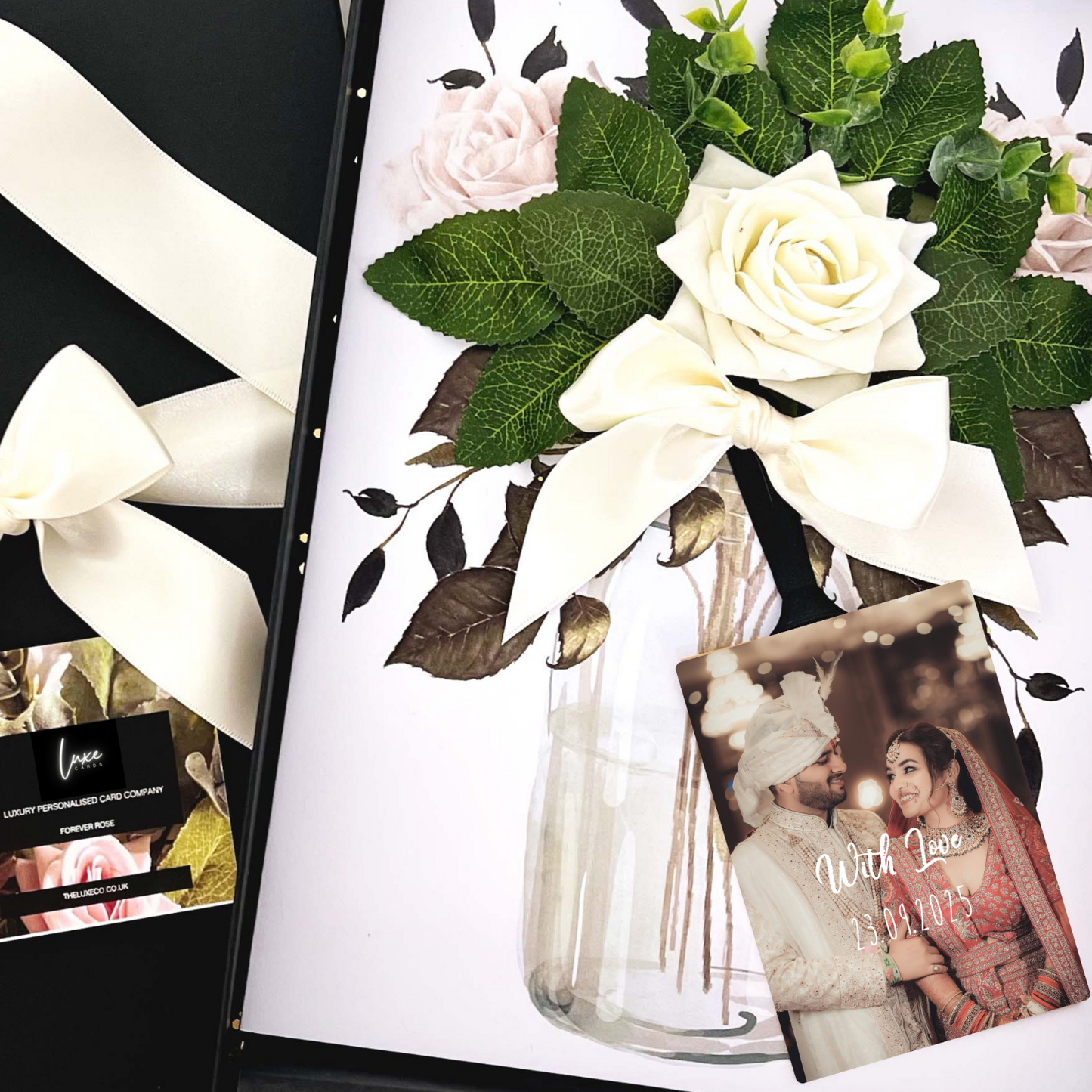 Sikh Personalised Wedding Card with Floral arrangement with white roses and green leaves in a clear vase, accompanied by a photo of a couple and a card.