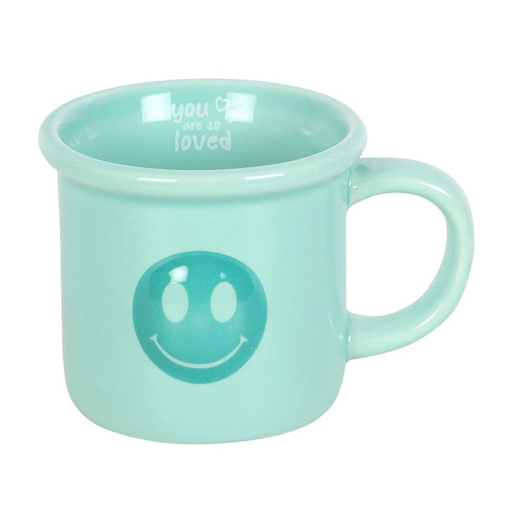 Mint green mug with smiley face design and text on a white background
