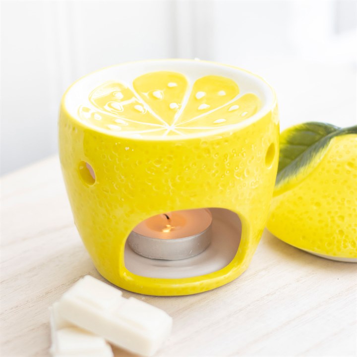 Yellow lemon-shaped wax warmer tealight candle holder for room fragrance oil with a lit tealight candle on a white surface.