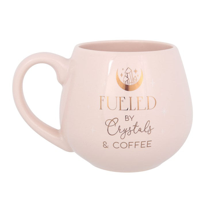 Pink mug with 'Fueled by Crystals & Coffee' text on a white background