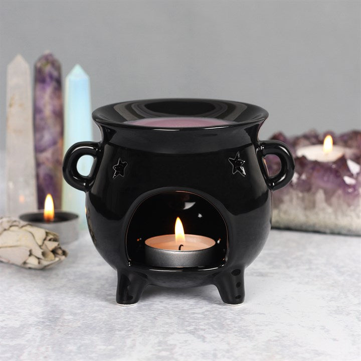 Witches cauldron wax warmer - a Black ceramic oil burner with a lit candle inside, surrounded by crystals and candles on a gray surface.