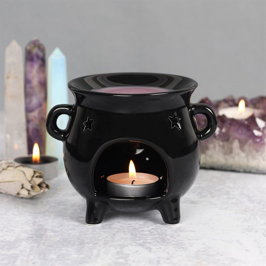 Witches cauldron wax warmer - a Black ceramic oil burner with a lit candle inside, surrounded by crystals and candles on a gray surface.