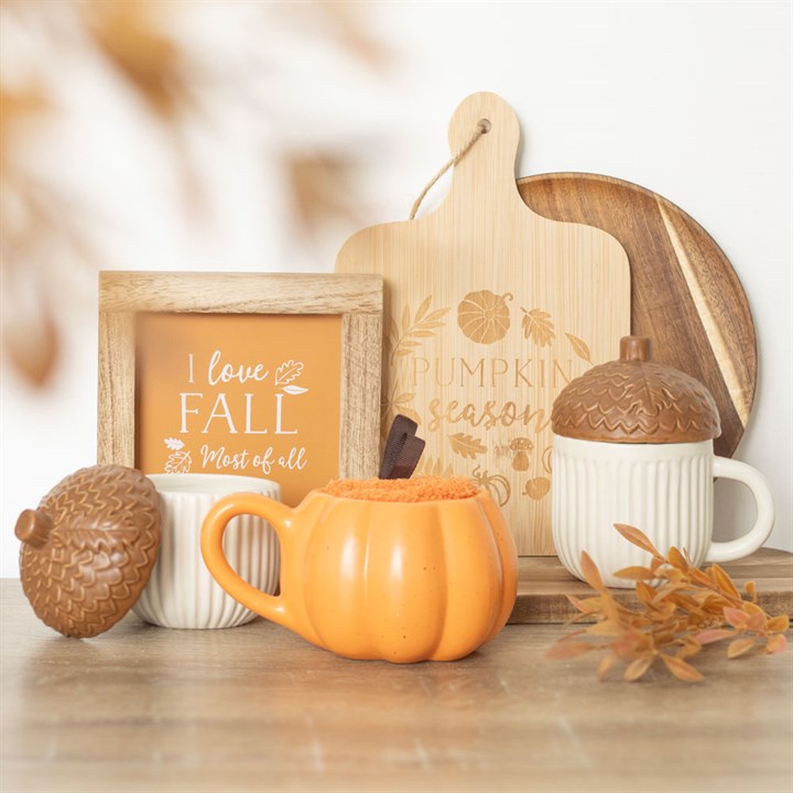 Autumn-themed decor with pumpkins, mugs, and a framed picture on a wooden surface.