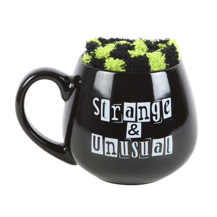 Black mug with 'Strange & Unusual' text and green checkered cozy on a white background