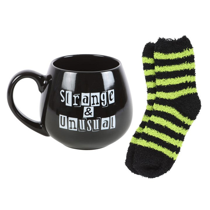 Black mug with 'Strange & Unusual' text and striped black and green sock on a white background