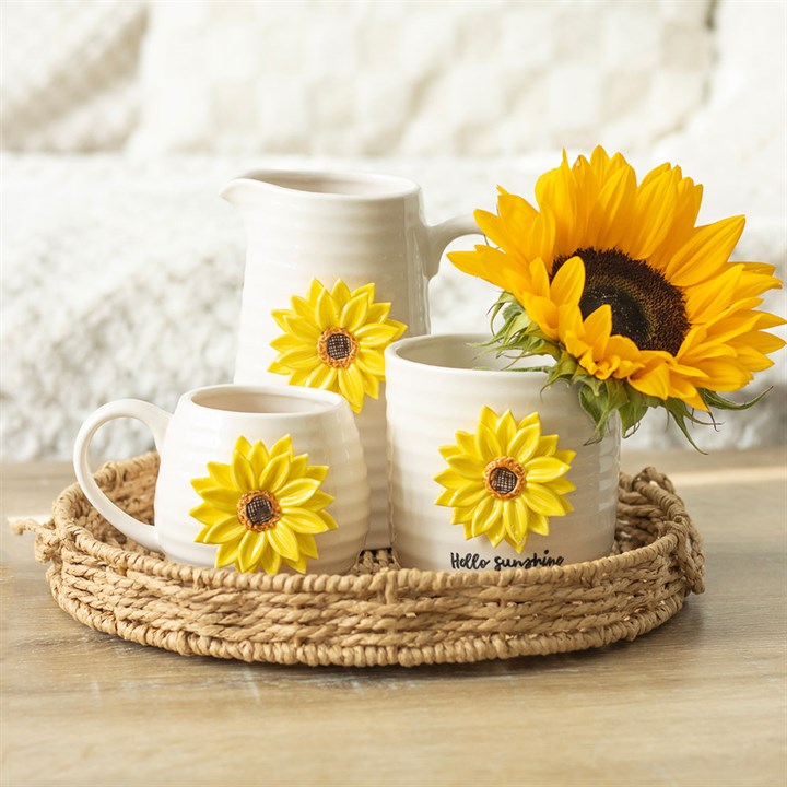 Set of white mugs with sunflower designs on a woven tray, with sunflowers on a blurred background.