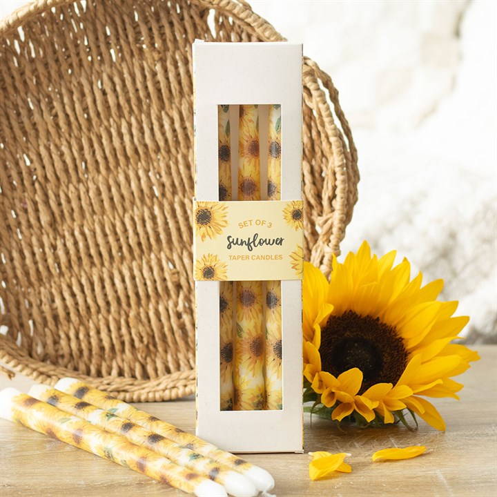 Sunflower-themed taper candles in a white box with a sunflower decoration, placed on a wooden surface.