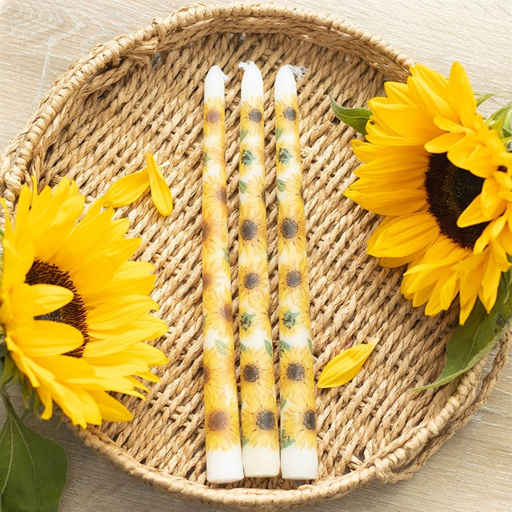 Three sunflower-patterned candles on a woven mat with sunflowers around