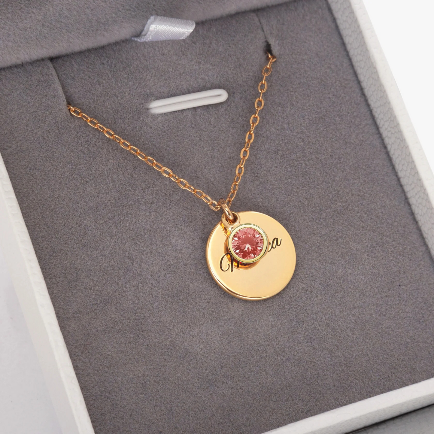 Gold necklace with a pink gemstone pendant on a gray background
