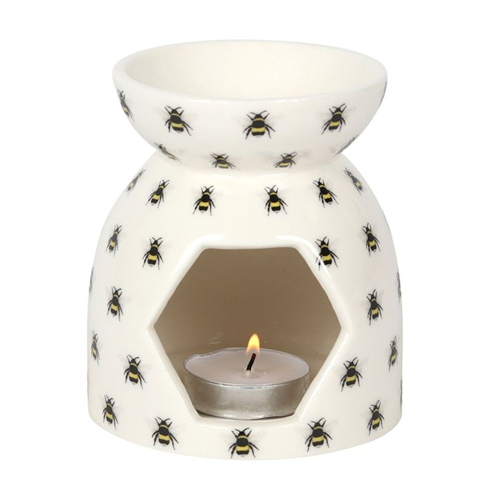 A white ceramic bee oil burner with an all-over bee print, featuring a hexagonal wax warmer on top and a lit tealight candle inside.