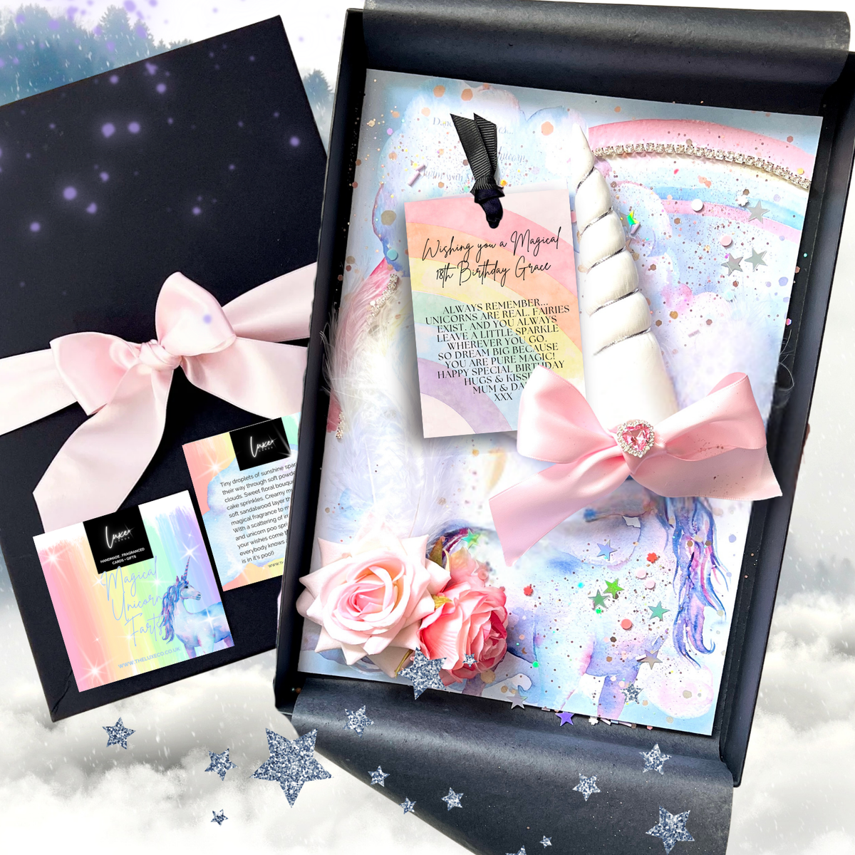 A magical 18th unicorn-themed birthday gift set displayed in a black box, featuring a pastel unicorn illustration, pink bows, rose decorations, and a small card. A matching black box with a pink bow is shown beside it on a soft cloud background.