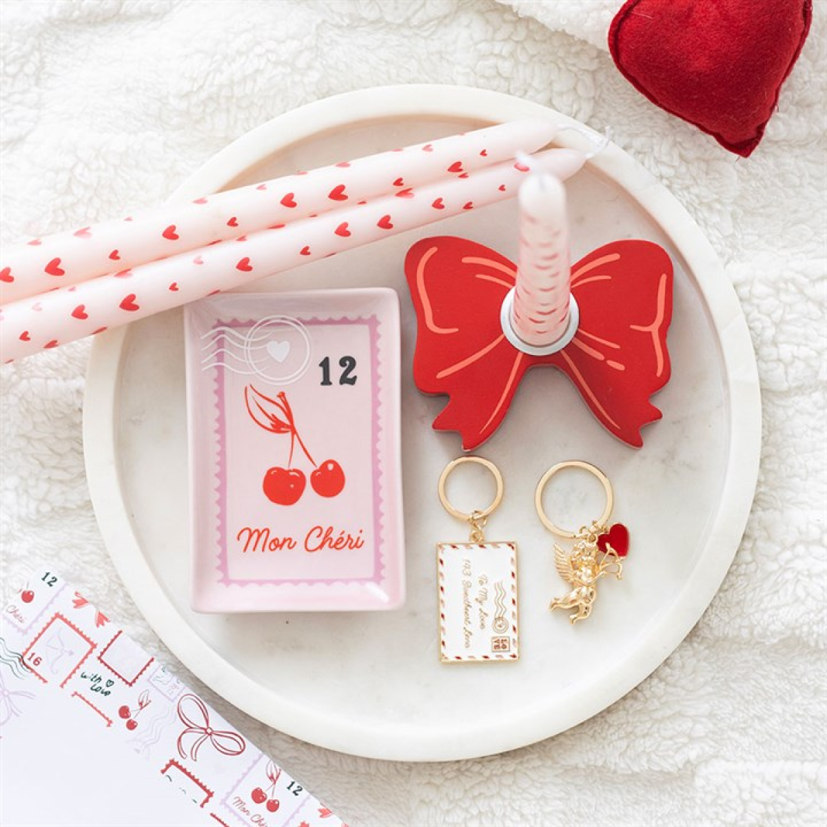 White plate with red bow, pink straws, keychain, and small box on a white surface.