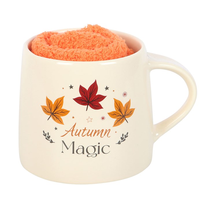 Mug with 'Autumn Magic' text and leaf designs, containing an orange fleece blanket.