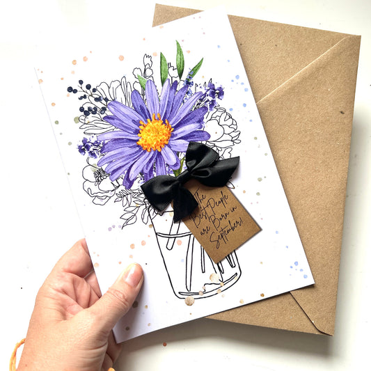 Aster greeting card featuring a purple aster watercolour painted artwork flower bouquet illustration with a black ribbon bow and kraft paper tag that reads 'The best people are born in September!'