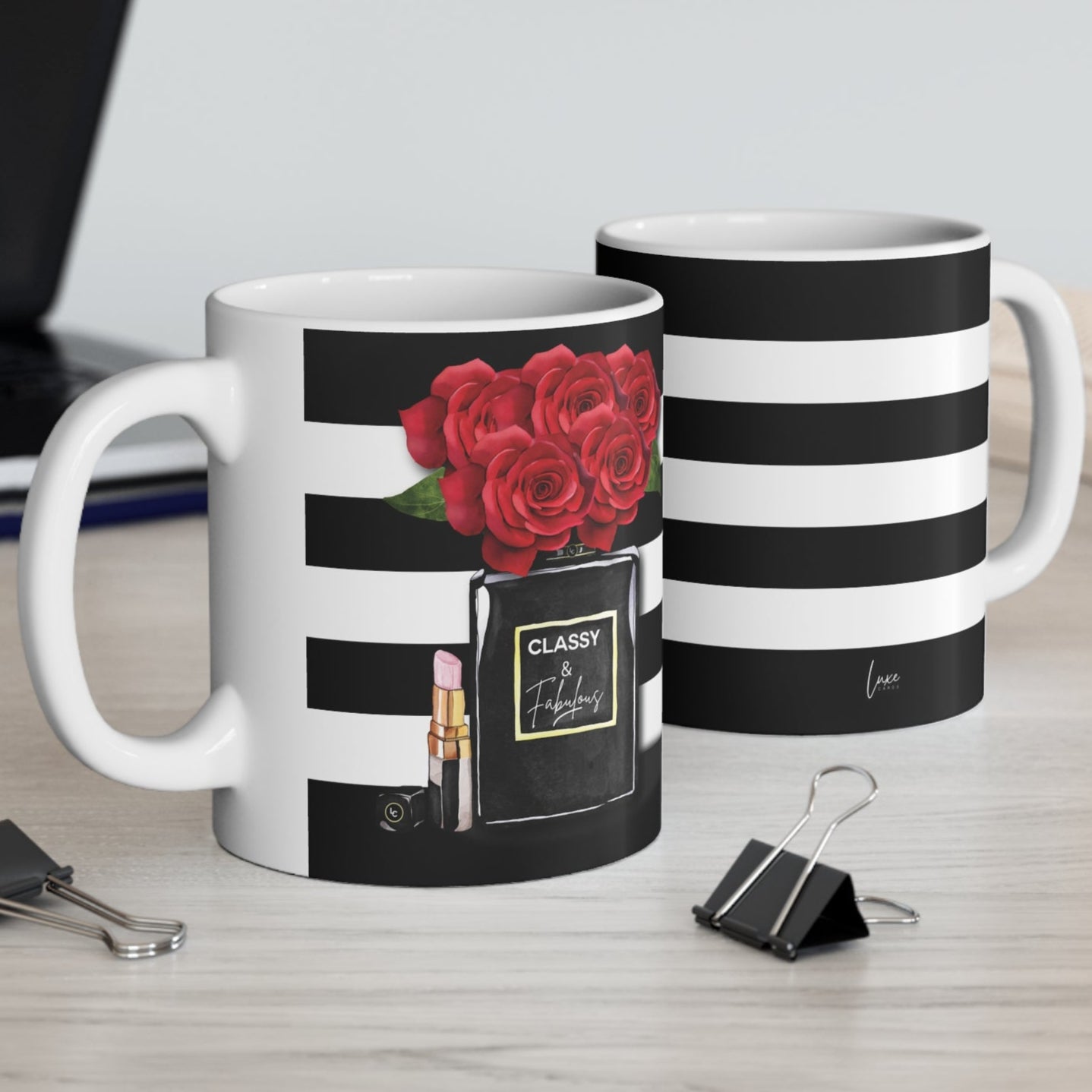 Two mugs on a desk with one featuring a rose design and the other with black and white stripes.