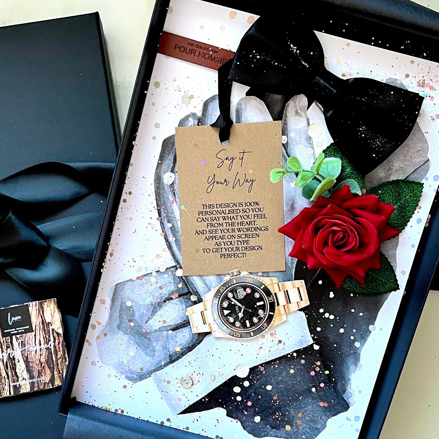 A luxury gift box handmade luxury personalised card for him presented on a velvet gift box. The set includes a black gift box with a black satin ribbon handmade with black bow tie, a gold-tone watch with a black dial, a everlasting red rose, and a 'Say Your Way' personalised printed wording card. Scented in masculine antique cologne for his birthday, anniversary for him