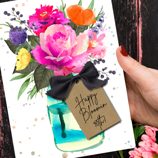 Happy Bloomin 90th Birthday Scented Hot Pink Rose A5 Card with envelope. A Cheery Greeting card that smells of rose for an experience rather than just a boring old card with colorful flowers, a mason jar, handmade with a 3d tag with satin bow reading 'Happy Bloomin' 90th' held by a hand.