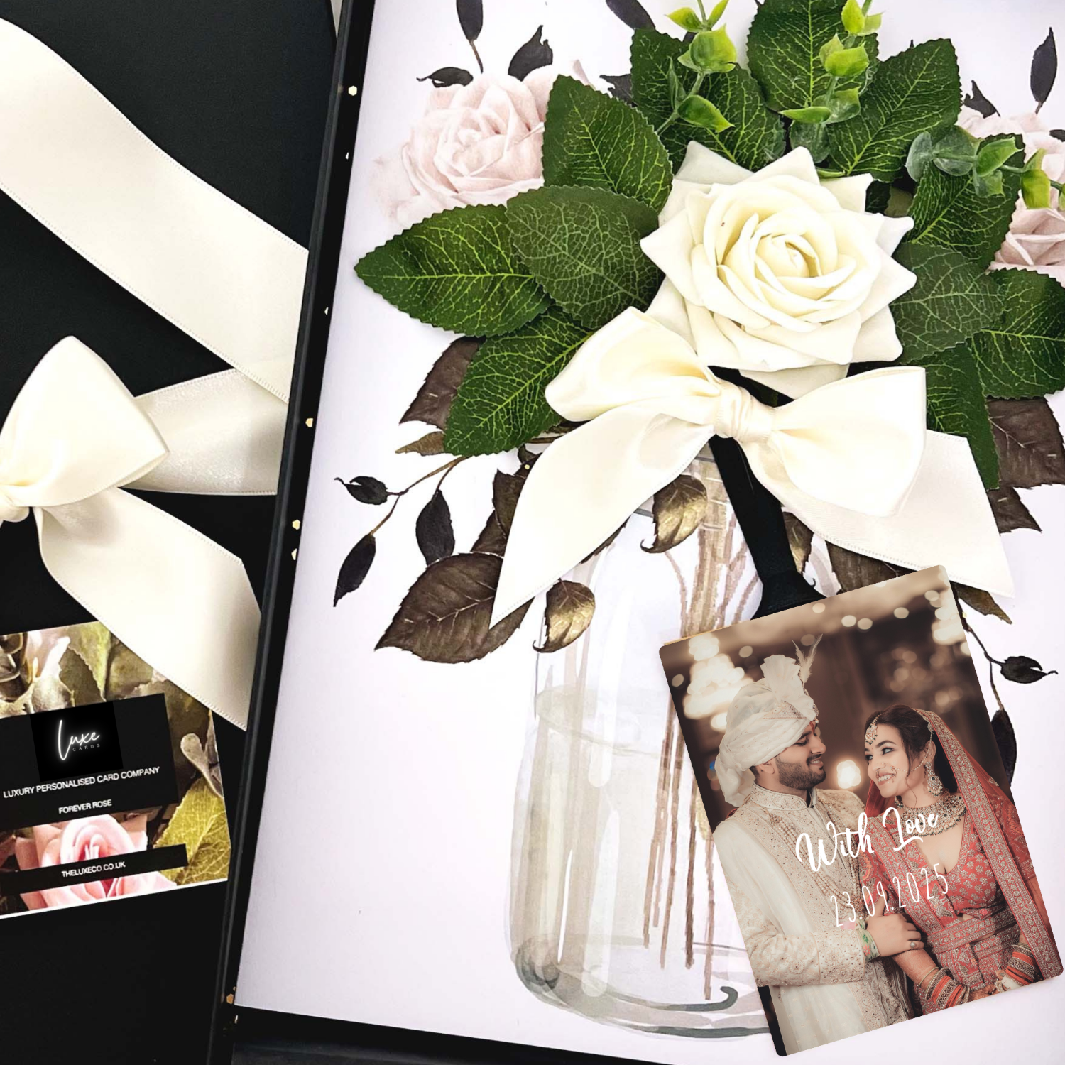 Sikh Personalised Wedding Card with Floral arrangement with white roses and green leaves in a clear vase, accompanied by a photo of a couple and a card.