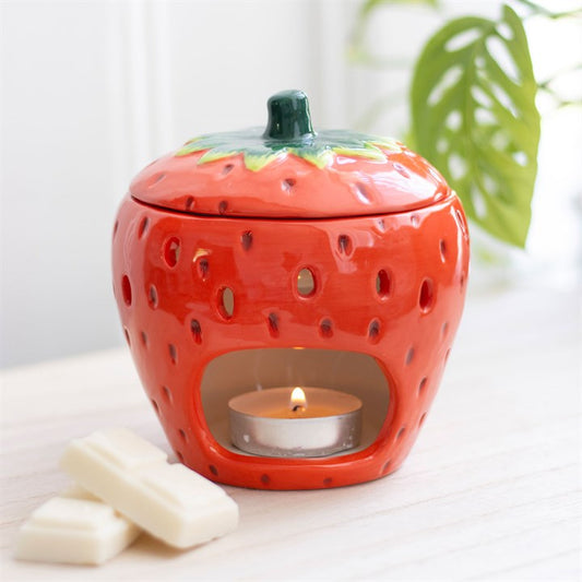 Strawberry-shaped ceramic oil burner with a lit candle inside on a white surface.