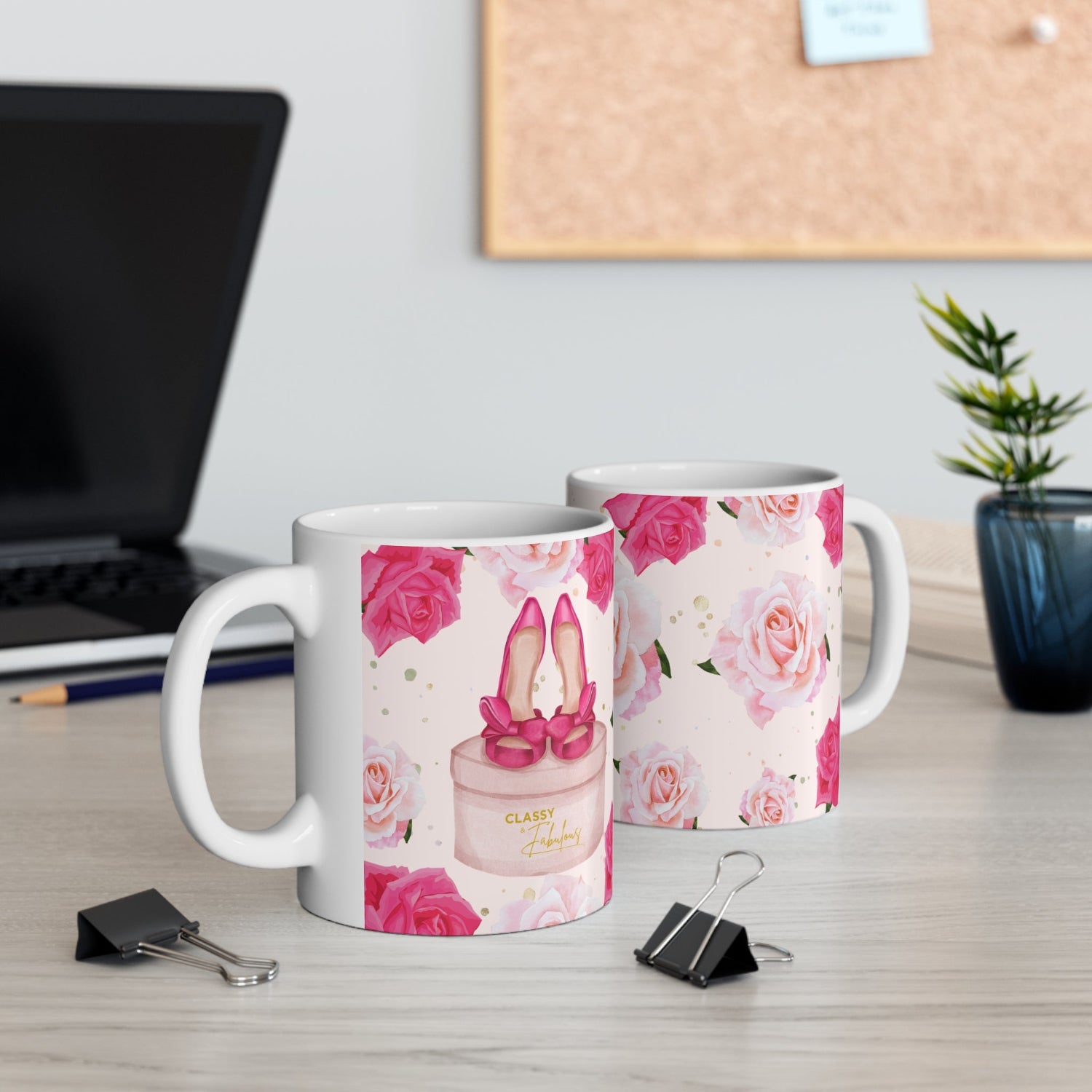 Two mugs with floral and high heel shoe designs on a desk with office items.