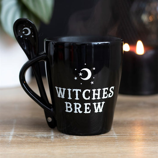 Black mug with 'Witches Brew' text on a wooden surface with a candle in the background