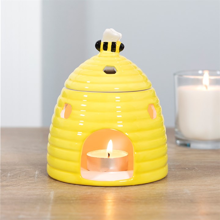 Yellow beehive ceramic bee tea light holder oil burner with a lit candle inside on a wooden surface.