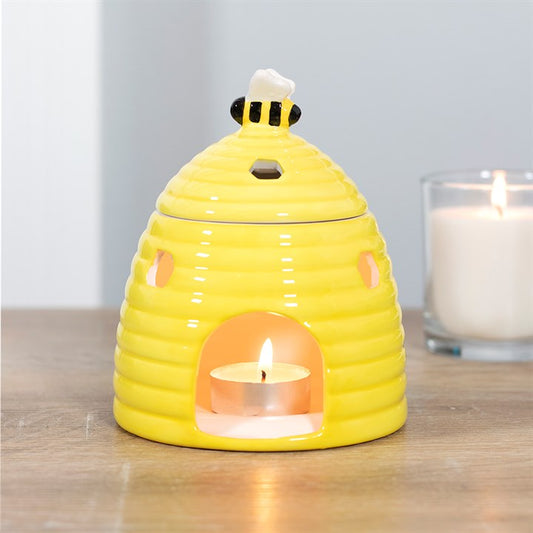 Yellow beehive ceramic bee tea light holder oil burner with a lit candle inside on a wooden surface.