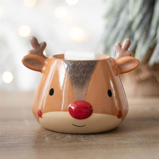 Reindeer-shaped tealight holder with a red nose on a wooden surface with blurred lights in the background