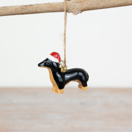 Sausage Dog Ceramic Hanging Xmas Decoration - Dog-shaped Christmas ornament with a Santa hat hanging on a branch.
