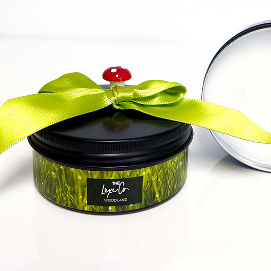 A black candle tin with green grass and toadstool design scented in woodland to match our woodland candle.
